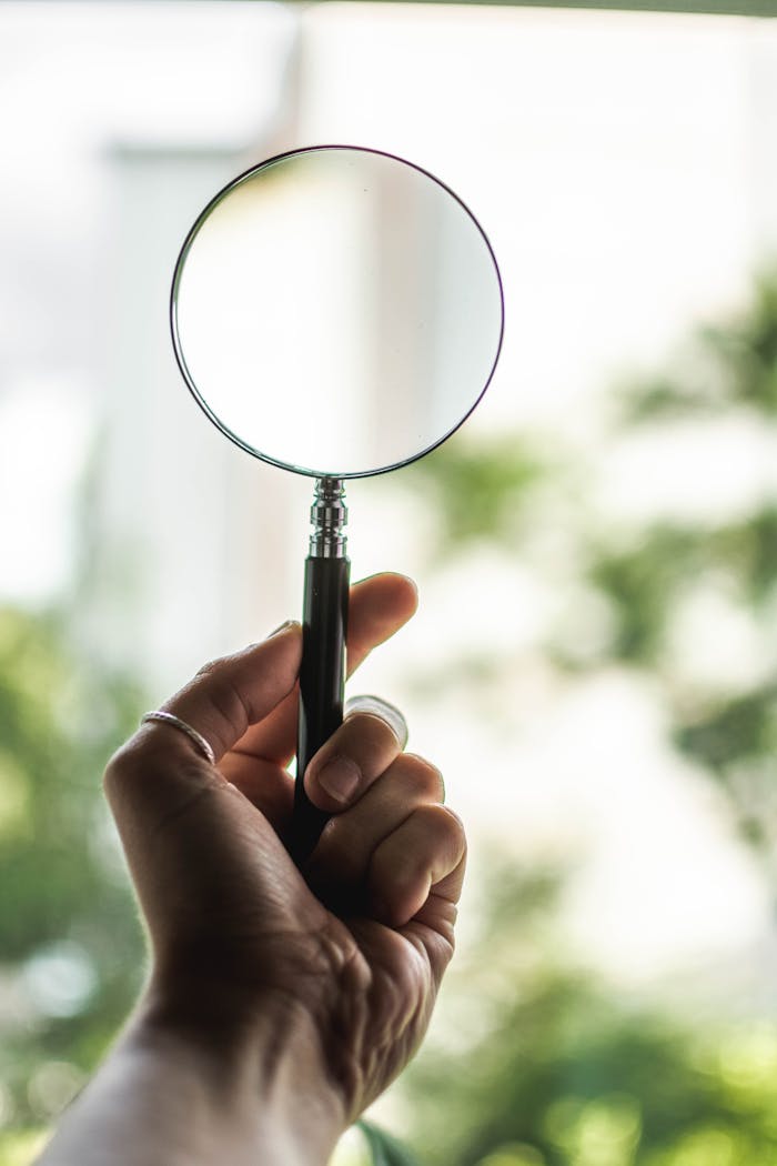 Close-up of a hand holding a magnifying glass on a sunny day outdoors.